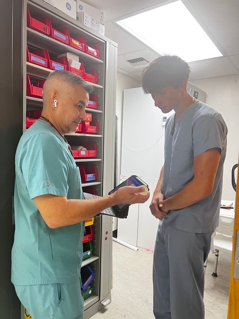 Two clinic team members reviewing inventory on a tablet in front of a supply cabinet